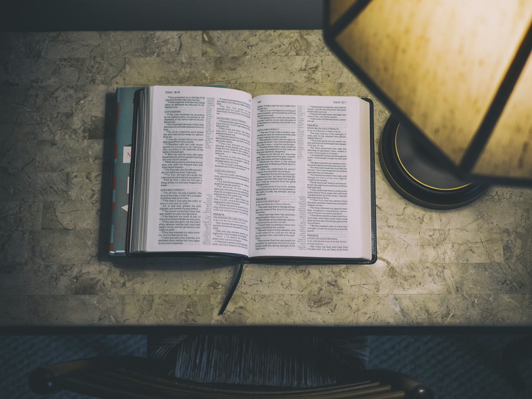 An open Bible on a table under a reading lamp